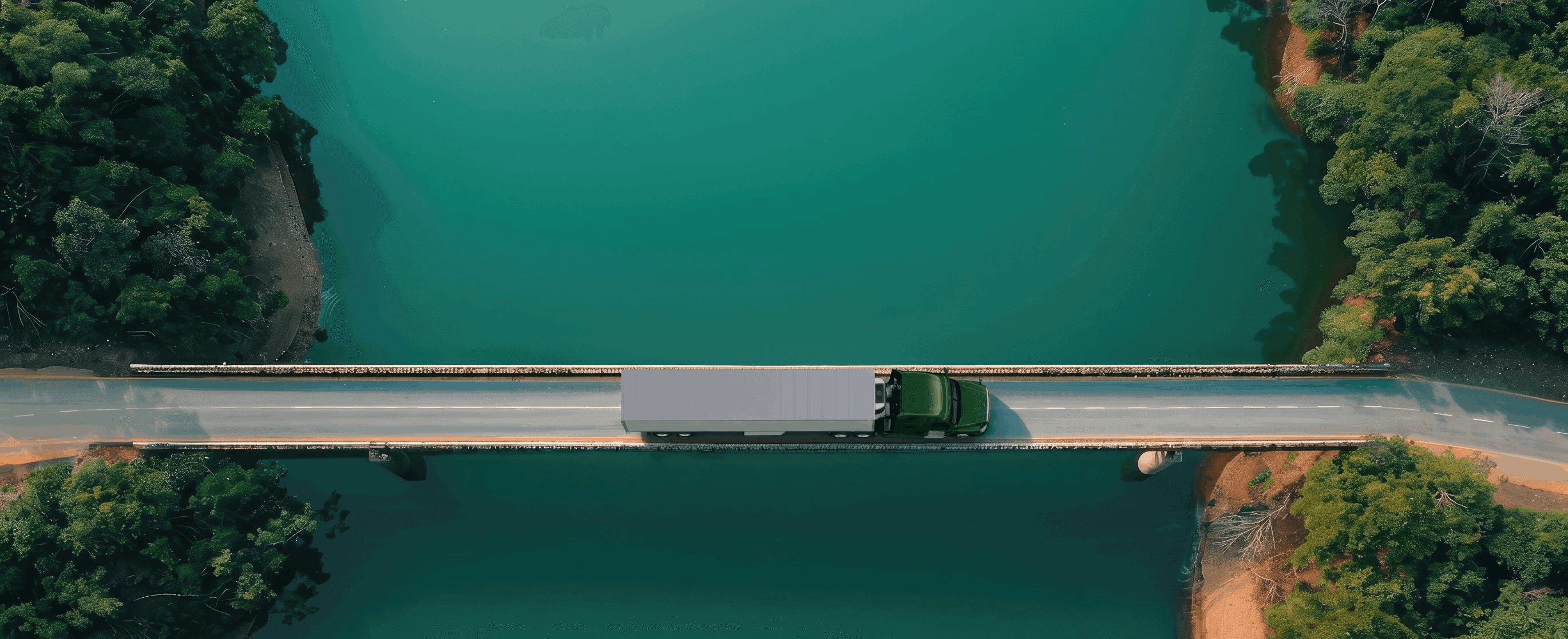 Aerial view of a semi-truck crossing a bridge over a river surrounded by forest