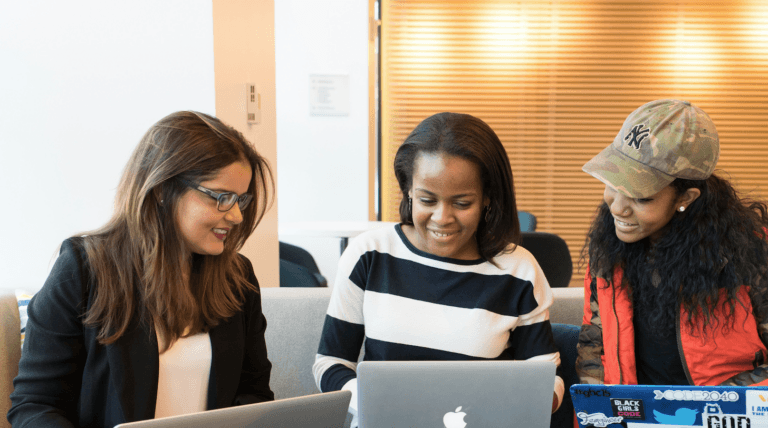 Three women collaborating around a laptop in a casual modern workspace with warm lighting