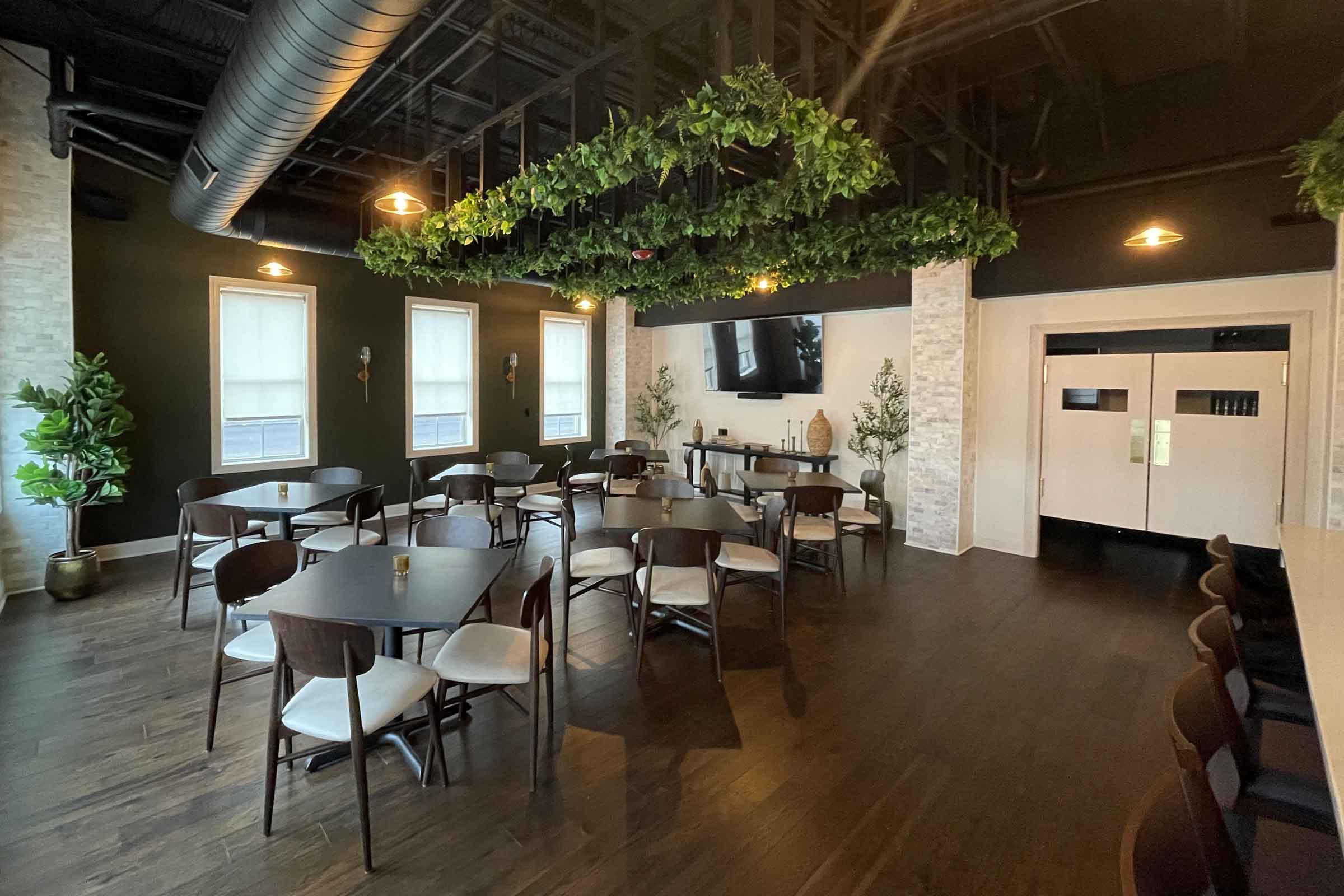 The Evergreen Room at Mezzo with small tables, a greenery canopy and double doors