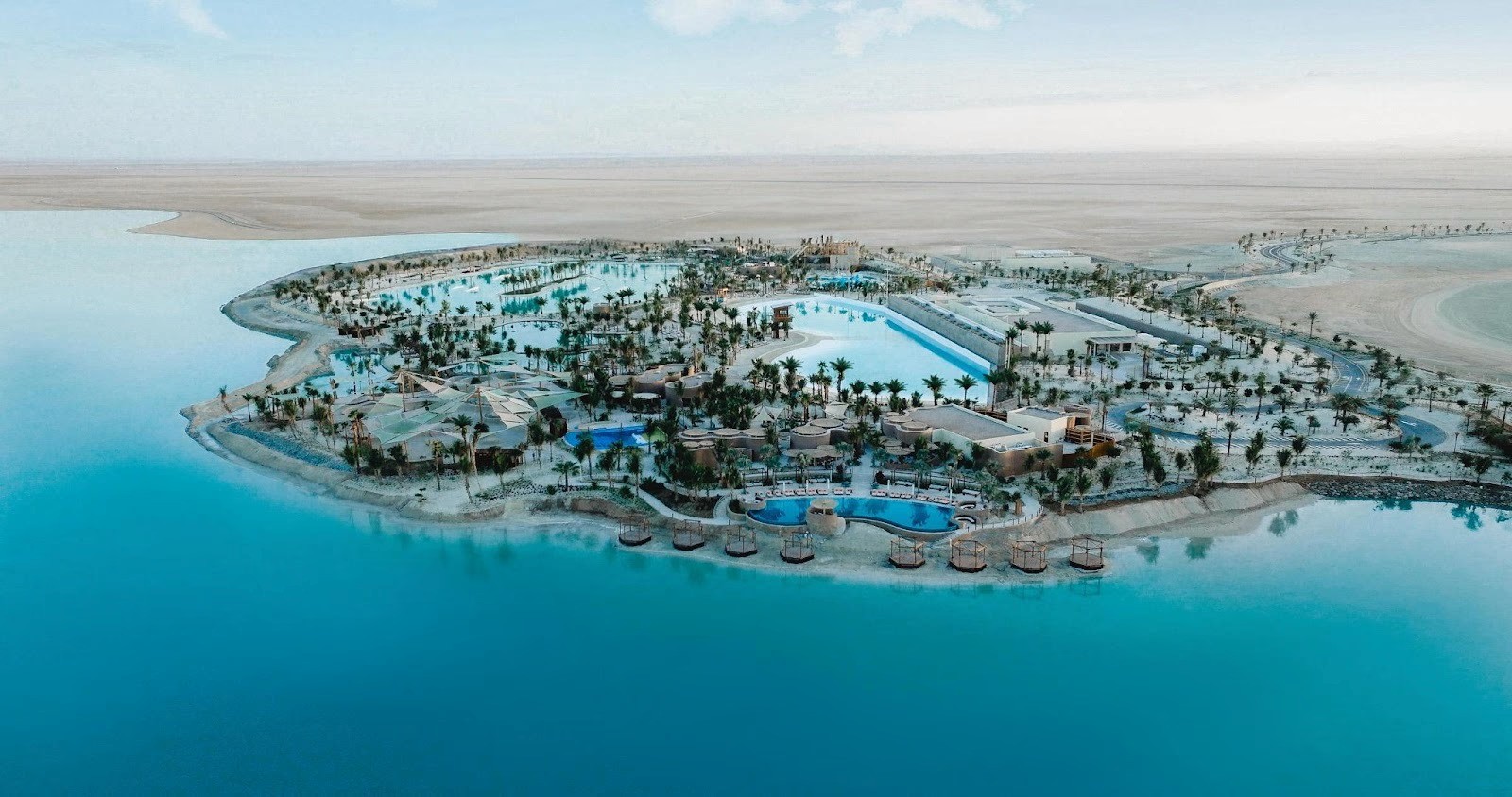 منظر علوي لمنتجع فاخر وسط جزيرة صحراوية بمياه فيروزية ونخيل، يجسد مفهوم الواحة العصرية التي تطورها شركة البحر الأحمر العالمية.