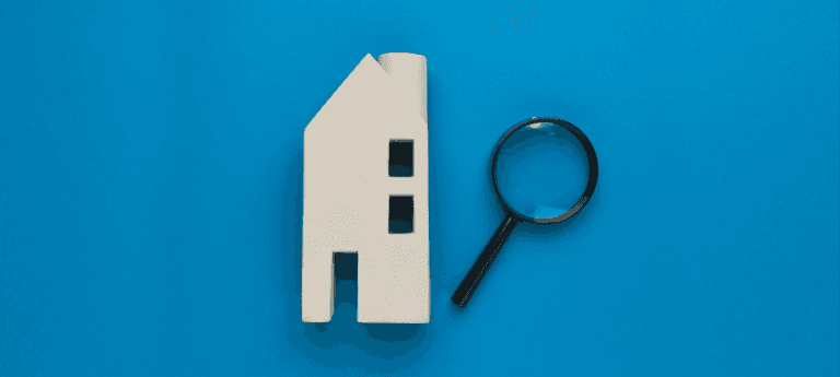 Model house and magnifying glass on a blue background, representing housing search or inspection.