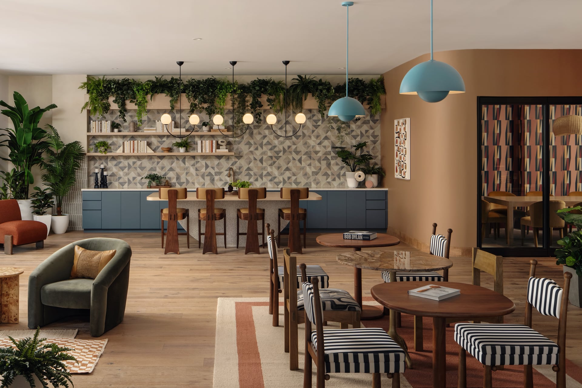Modern commercial interior design featuring a cafe lounge, wooden seating with black-and-white striped cushions, blue dome lights, and indoor plants.