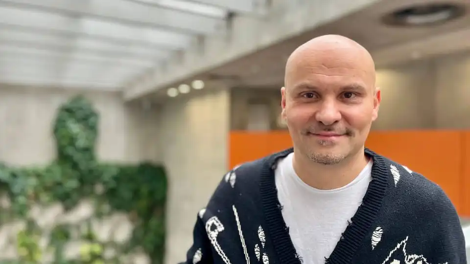 Smiling man indoors with plants in the background.