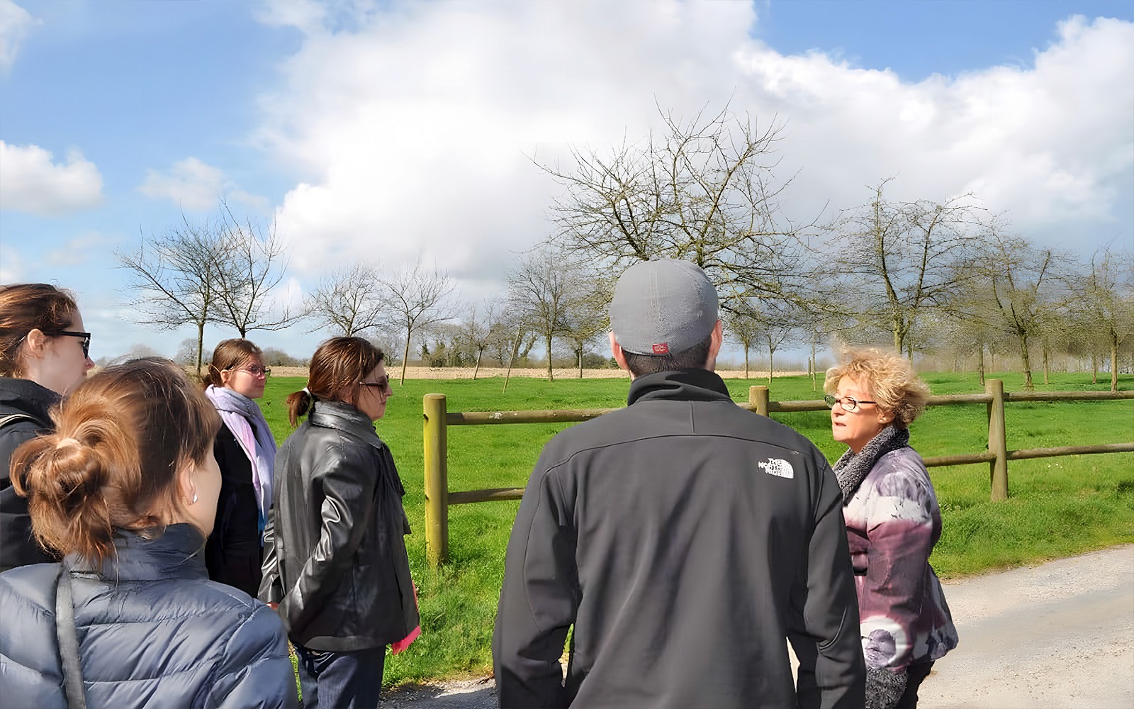 Tour group listening to a guide at Normandy, France, with green fields and trees in the background.