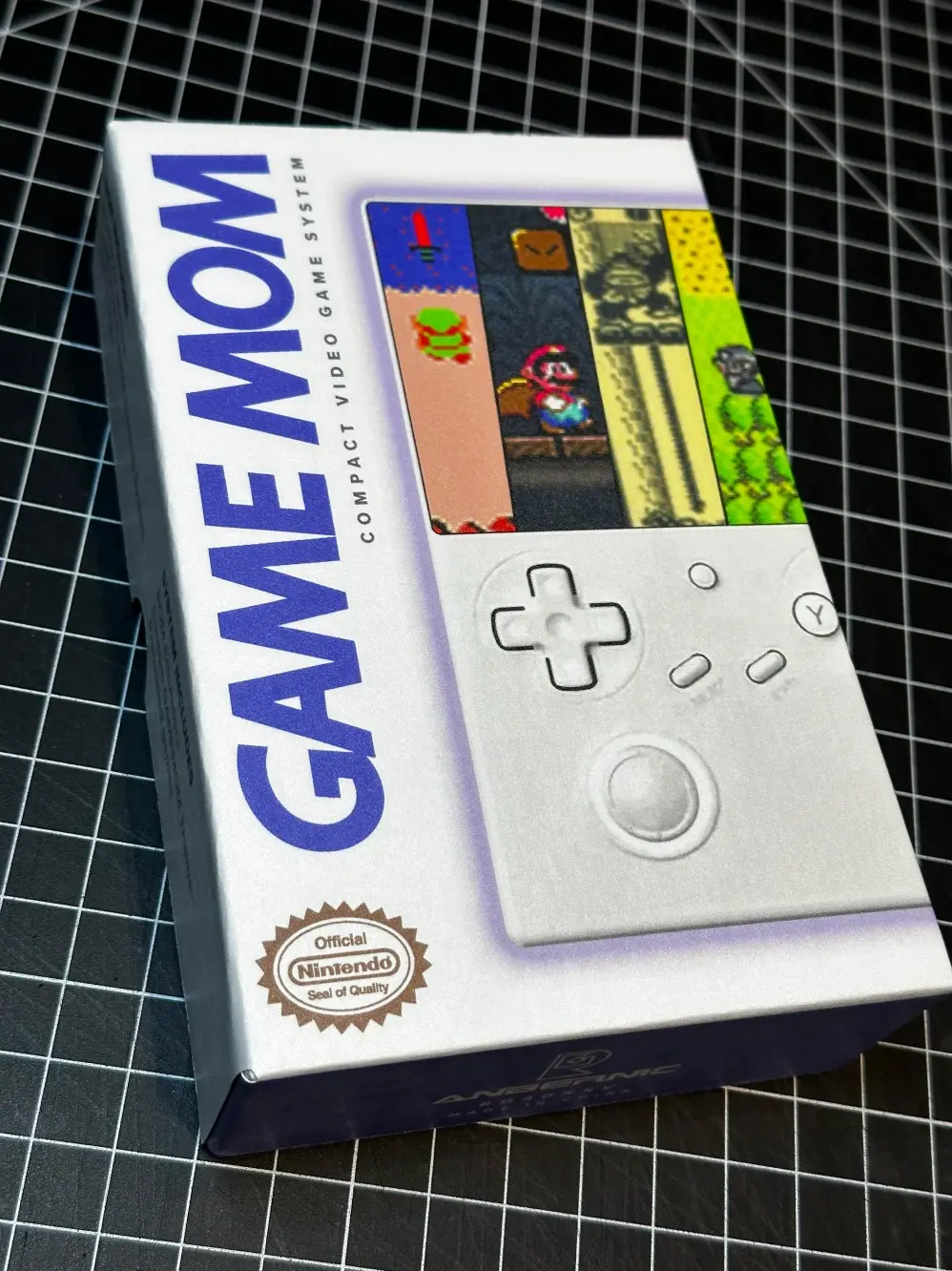 The image features a boxed "Game Mom" compact video game system, displaying retro video game graphics on the packaging, with a sleek white controller design prominently shown. Rob Harrigan Design. Rob Harrigan. 