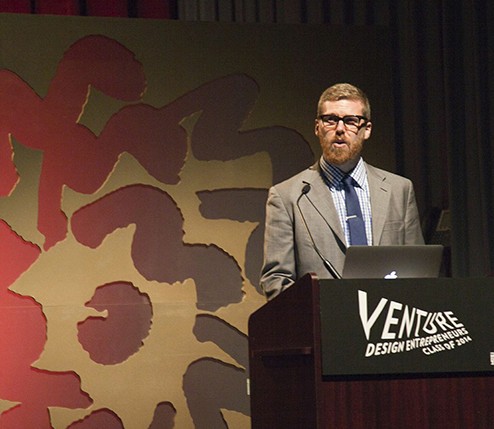 portrait of a man in a suit and tie giving a speech from a stand