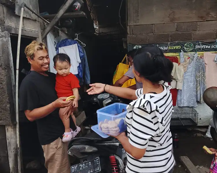 Volunteer gives food donations to a smiling father holding his toddler at home in their village