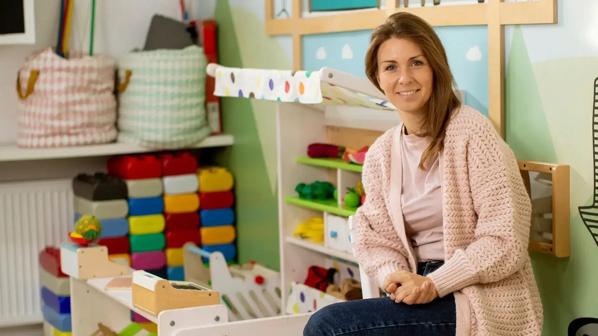 A teacher smiling to the camera in front of toys