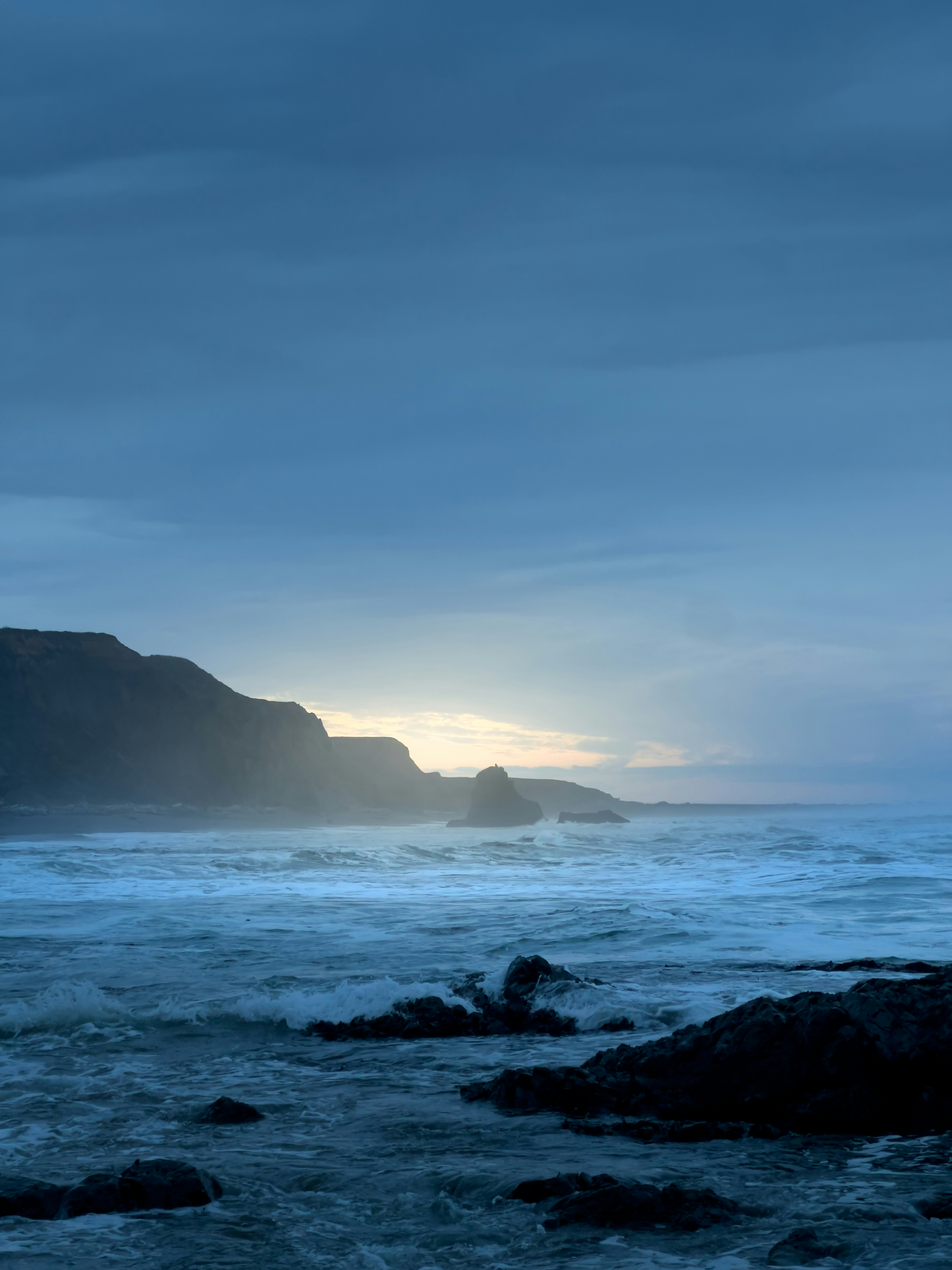 Waves crash on rocky shore under cloudy sky