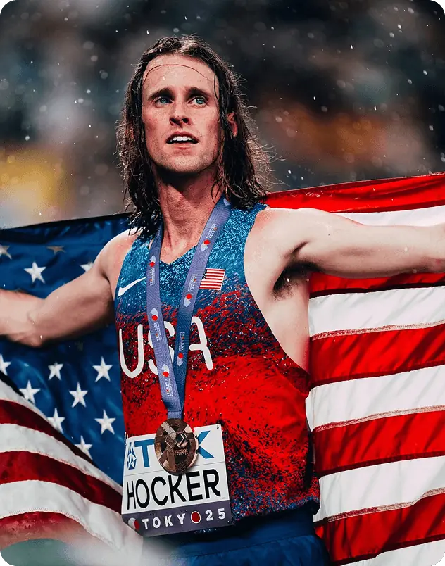 Male athlete with long hair holding a U.S. flag, wearing a Rythm device on his upper arm.