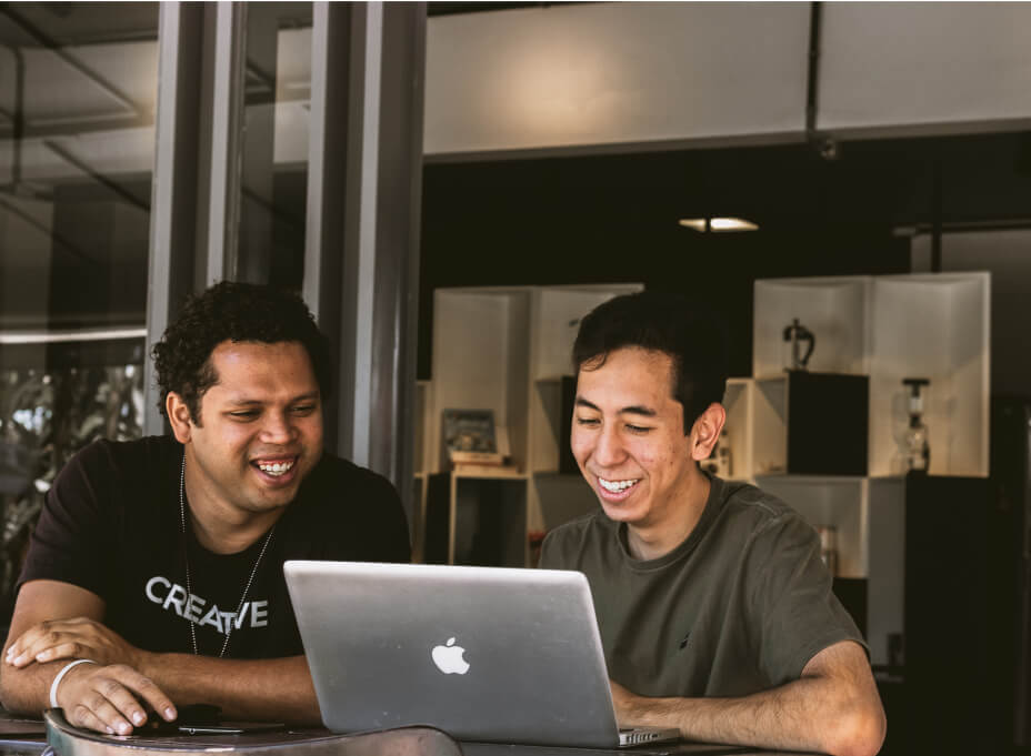 Two men working together on a laptop laughing and enjoying themselves after getting a green card visa.