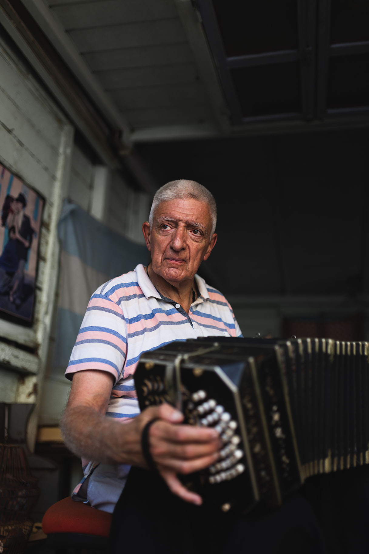 Portrait of an old man playing the accordion inside a small home.
