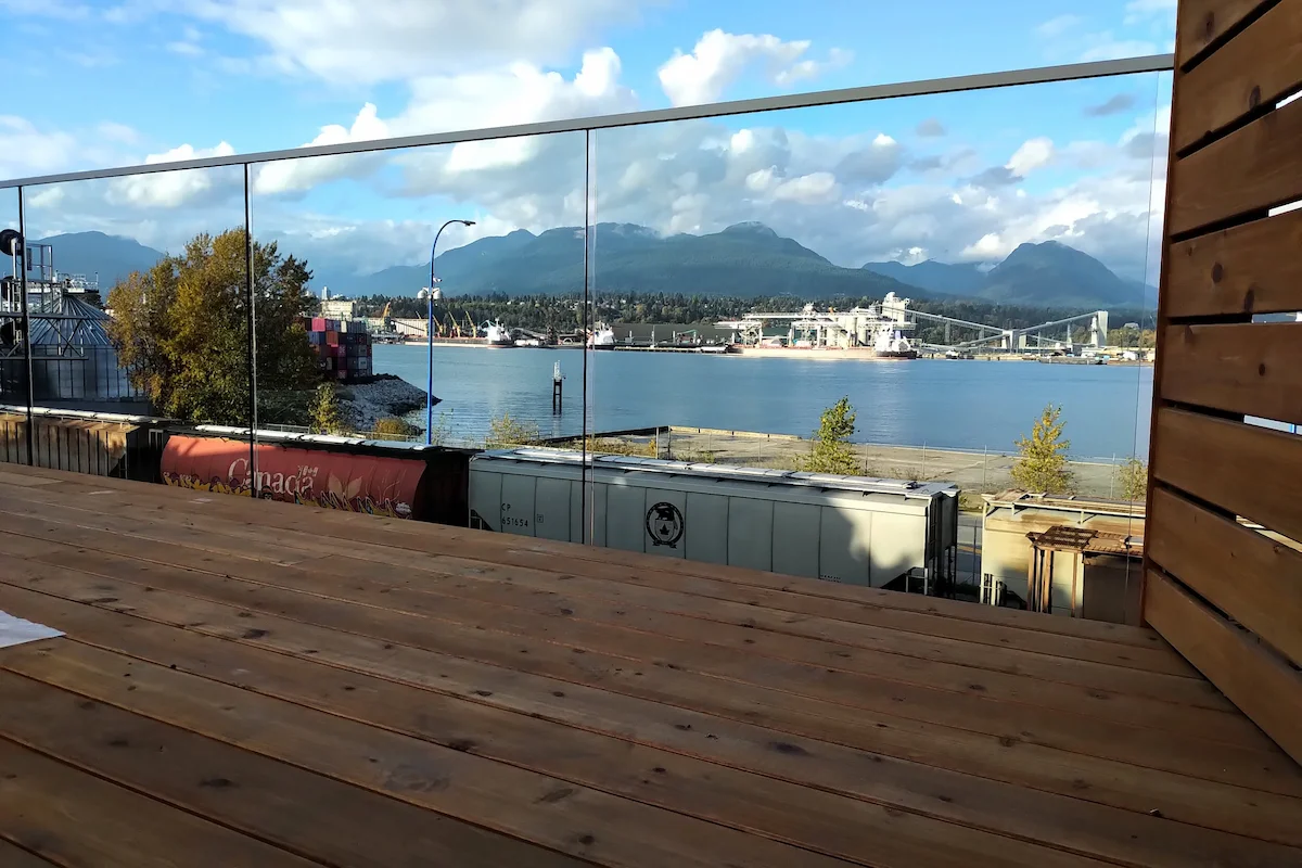 Wood patio deck in Vancouver featuring clear glass railing panels that reduce wind exposure while maintaining open sightlines to the waterfront and mountains.