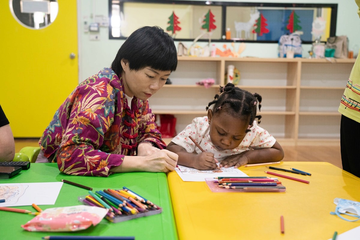Teacher and child drawing together at a bright classroom table