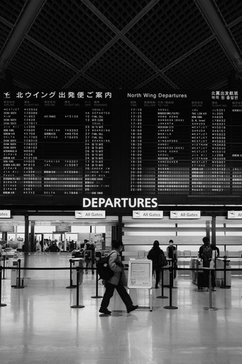 People walk past a departure board in an airport illustrating the pre departure checklist