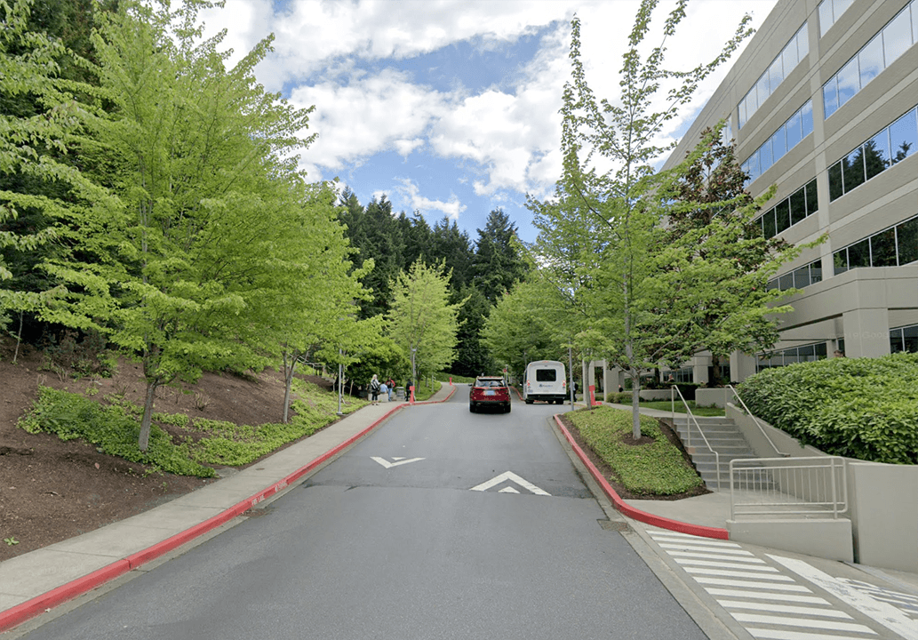 A generic corporate building situated along a vehicular road, surrounded by steep, planted slopes that highlight the disjointed and inaccessible layout of T-Mobile's campus.