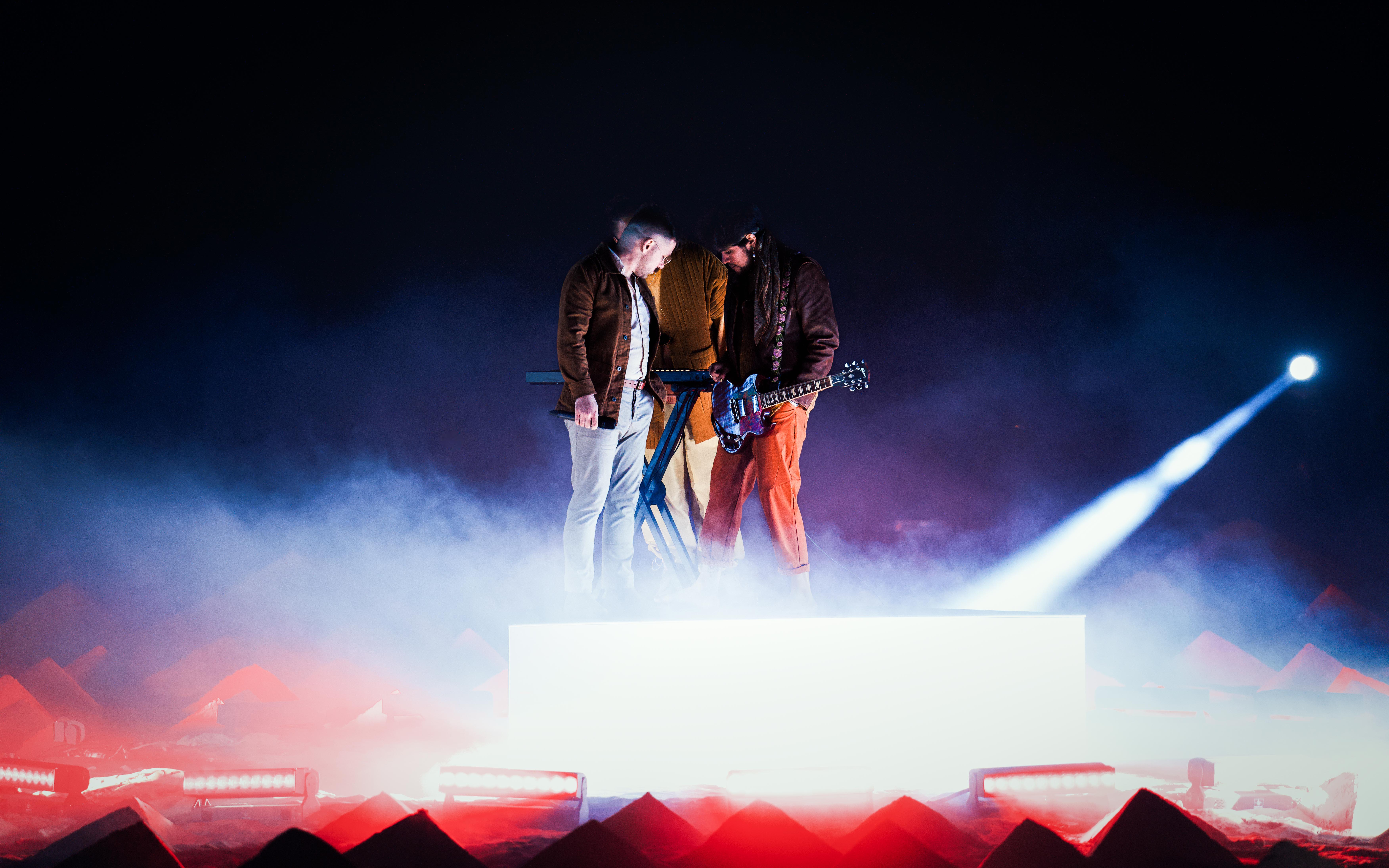 The band A R I Z O N A standing on a mirrored stage while shooting a music video for the song “Moving On” directed by Owen Brown