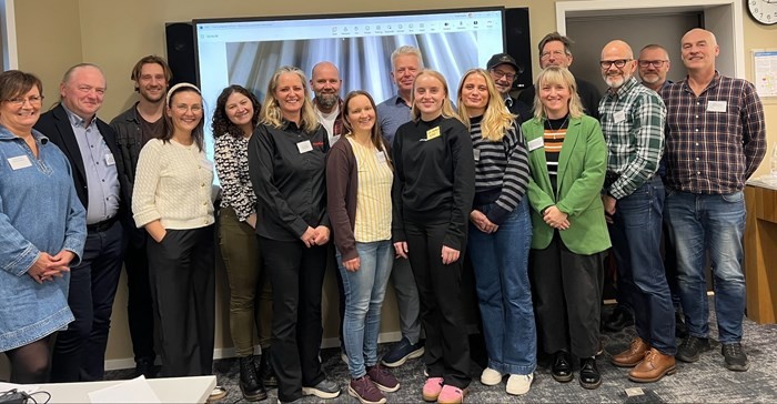 Group of people standing together in a room, posing for a photo with a presentation screen in the background.