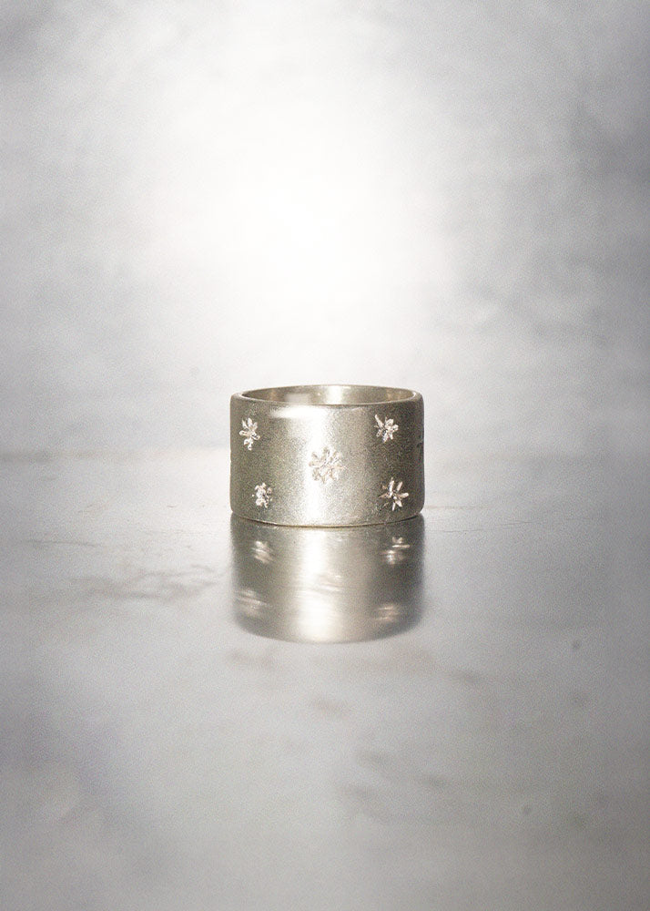 Silver ring with engraved sparks on a reflective gray surface