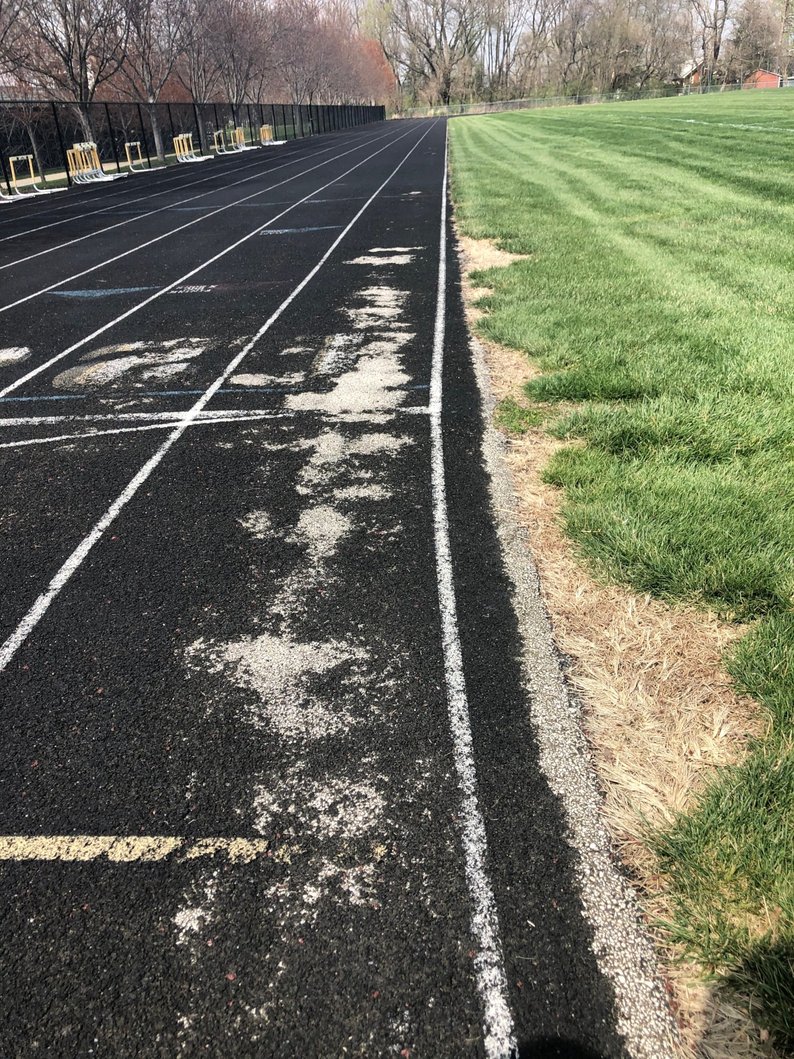 Damaged running track with visible cracks and texture loss, an example of track drainage problems and surface failure.