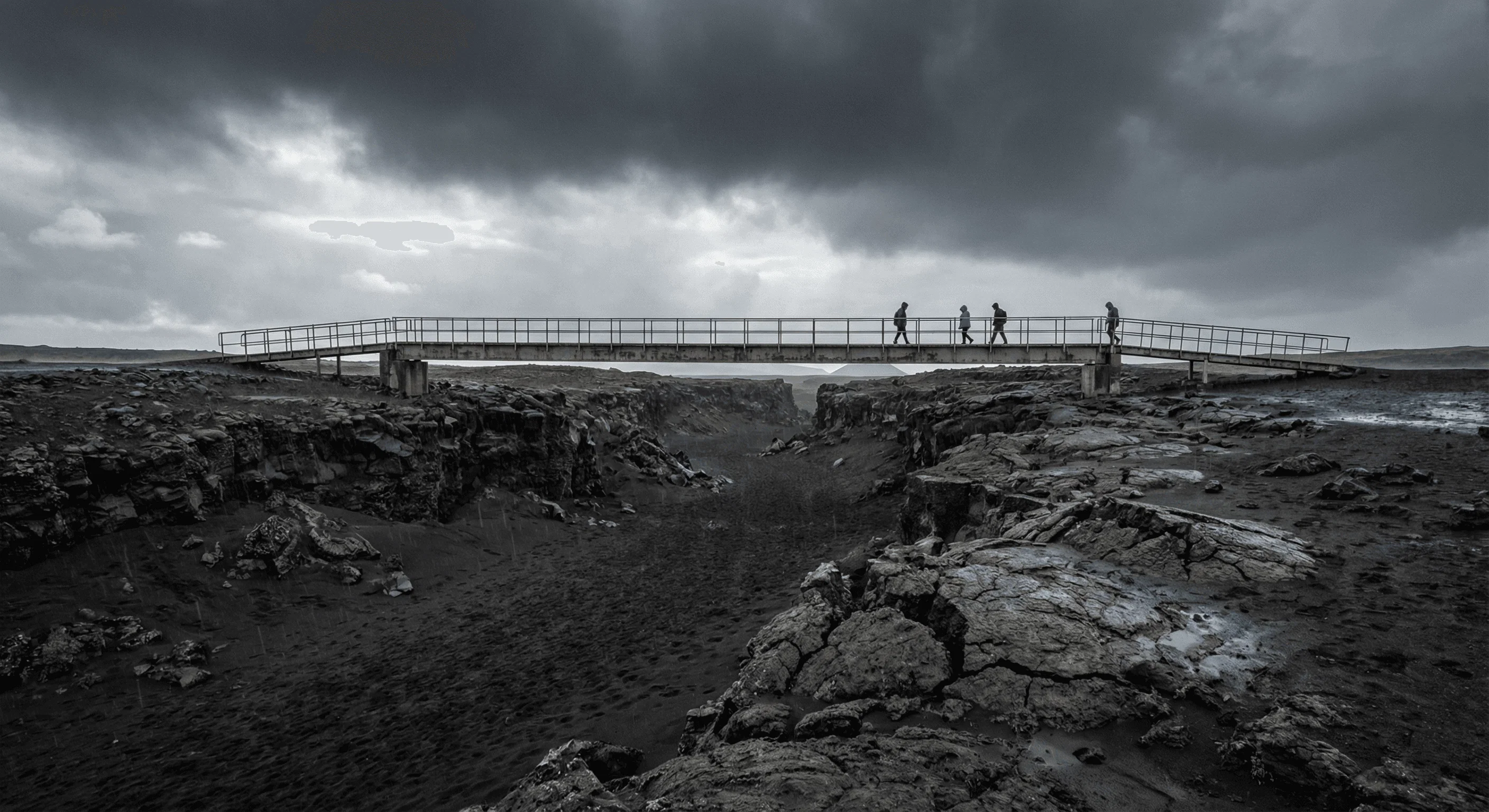 People walking on a metal footbridge spanning a rift between two rocky tectonic plates.