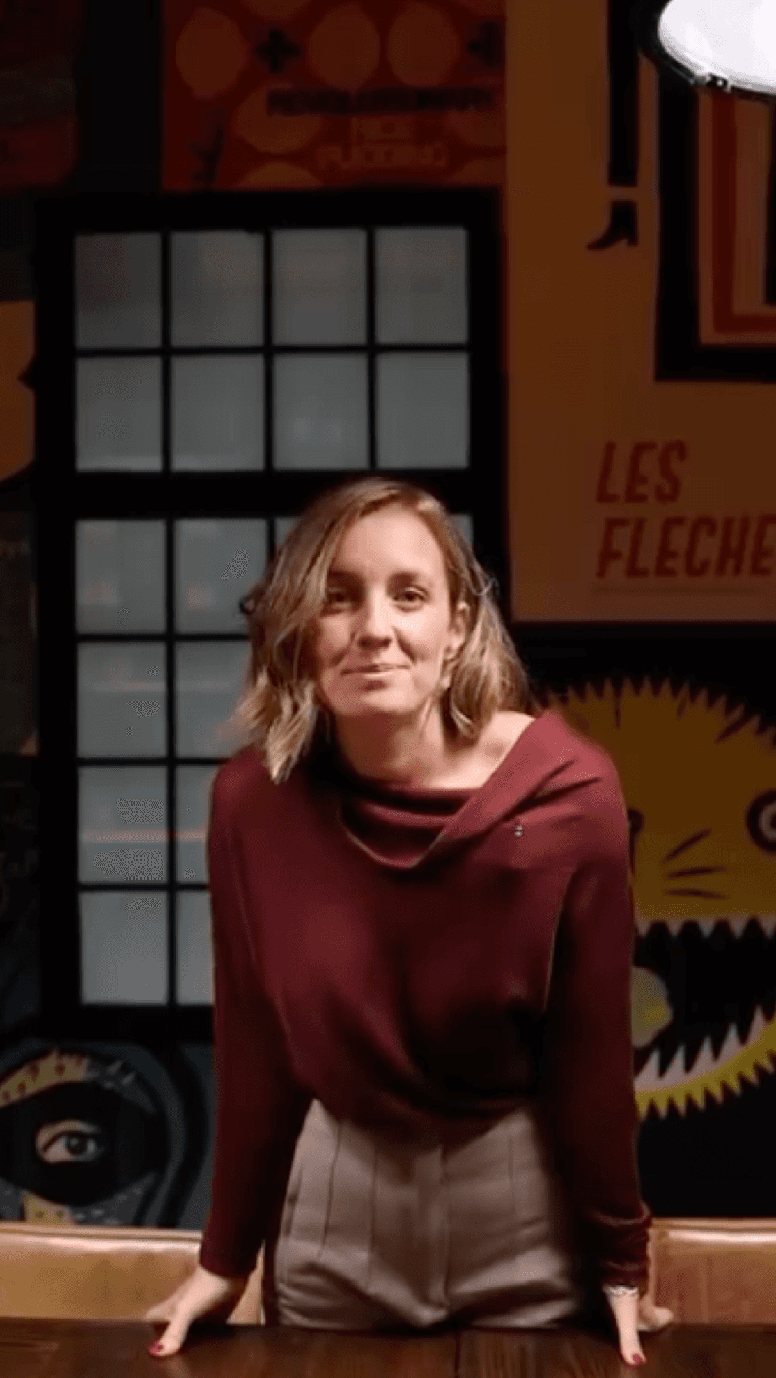 Mujer sonriente posando en El Privado frente a una pared decorada con carteles y una ventana de cuadrícula