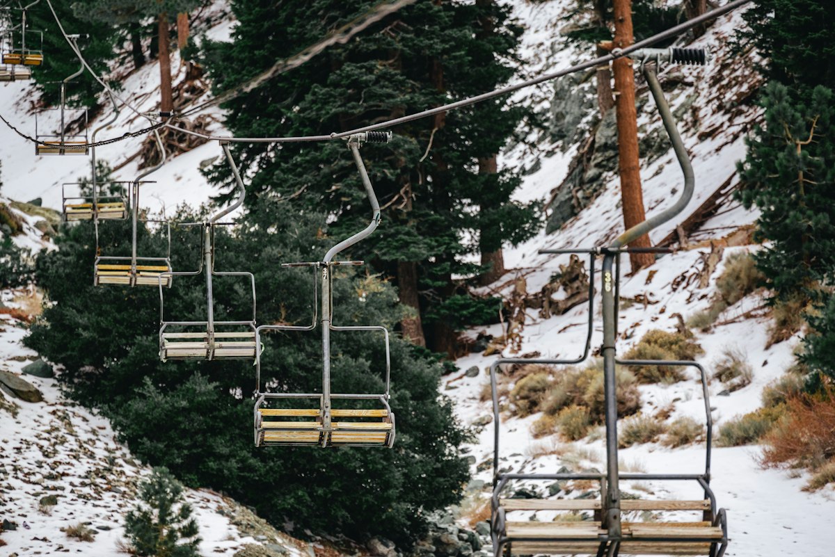 Empty chairlift chairs hanging above snow-covered pine trees on a clear morning