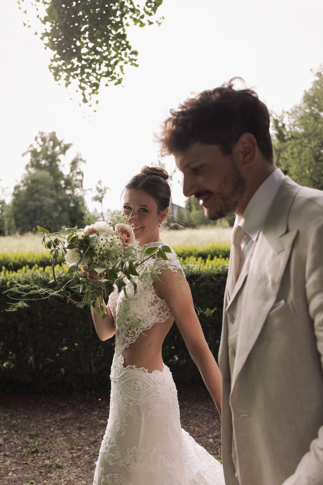 Sposi alla Rocca di Soragna, lei con bouquet di gypsophila, lui in lino beige, si guardano nel giardino dopo la cerimonia