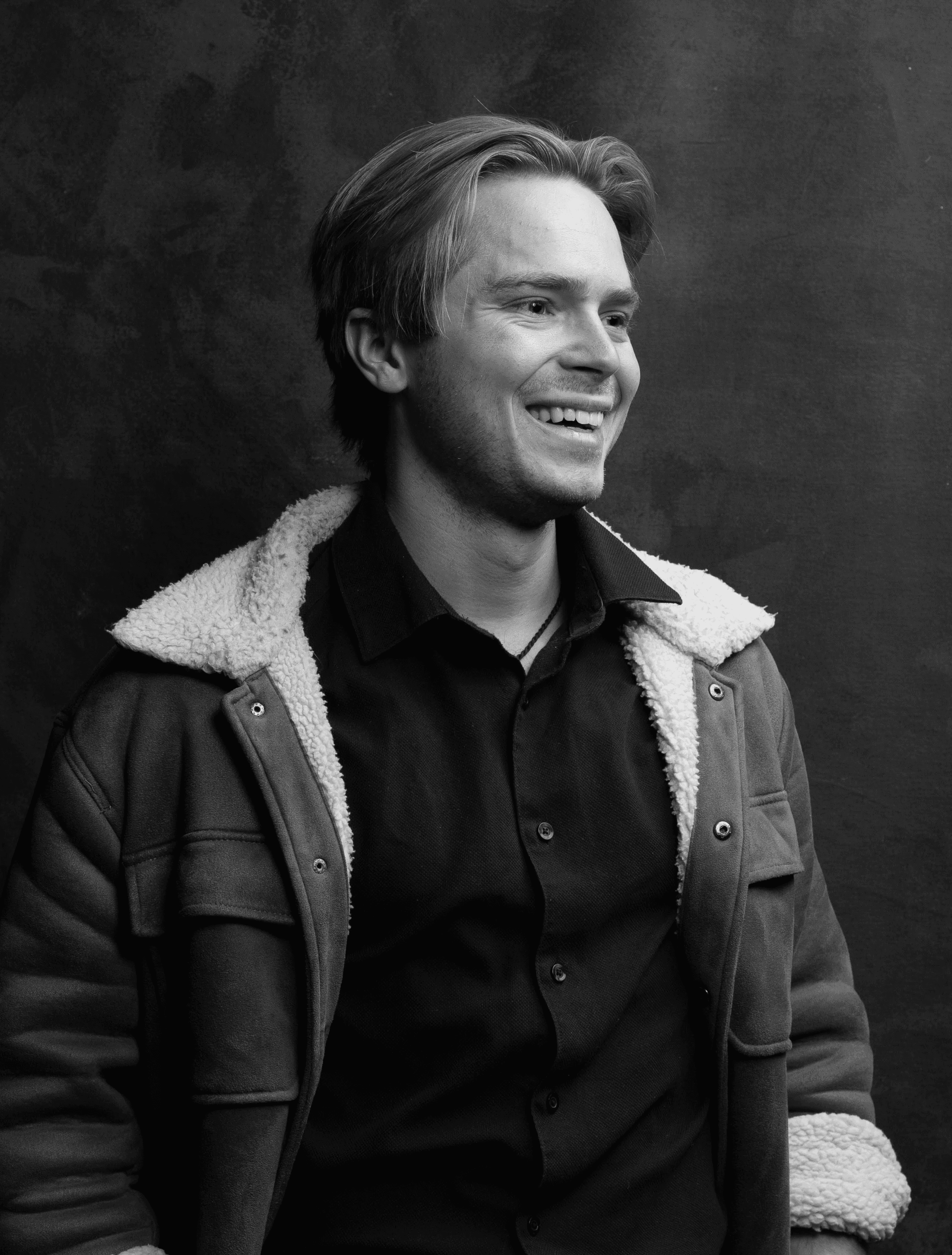 Portrait of a man with short dark hair and a trimmed beard, dressed in a dark shirt, on a simple background.