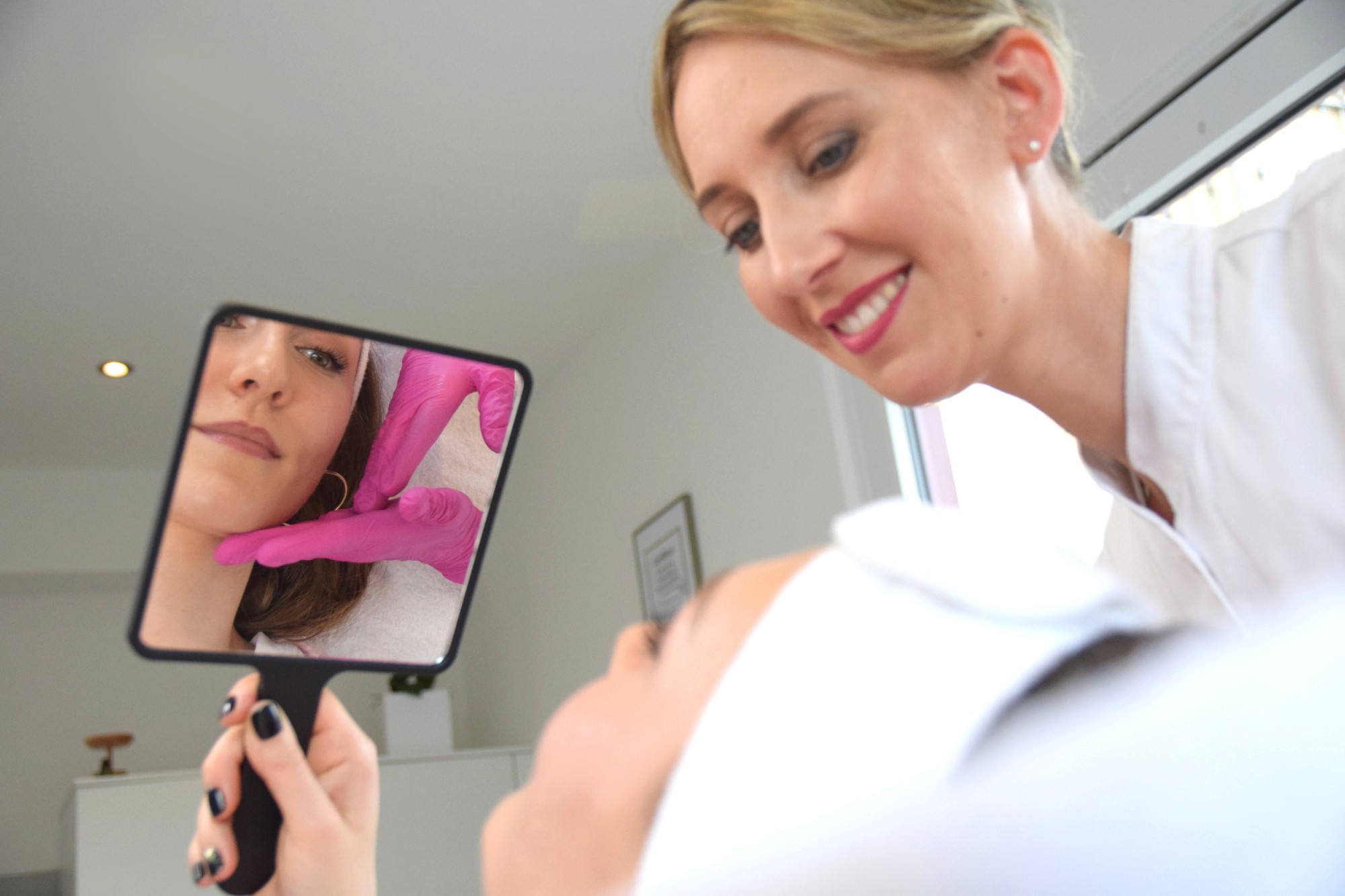 Frau blickt zufrieden in den Spiegel – gesundes, strahlendes Hautbild nach Gesichtsbehandlung durch Heilpraktikerin.