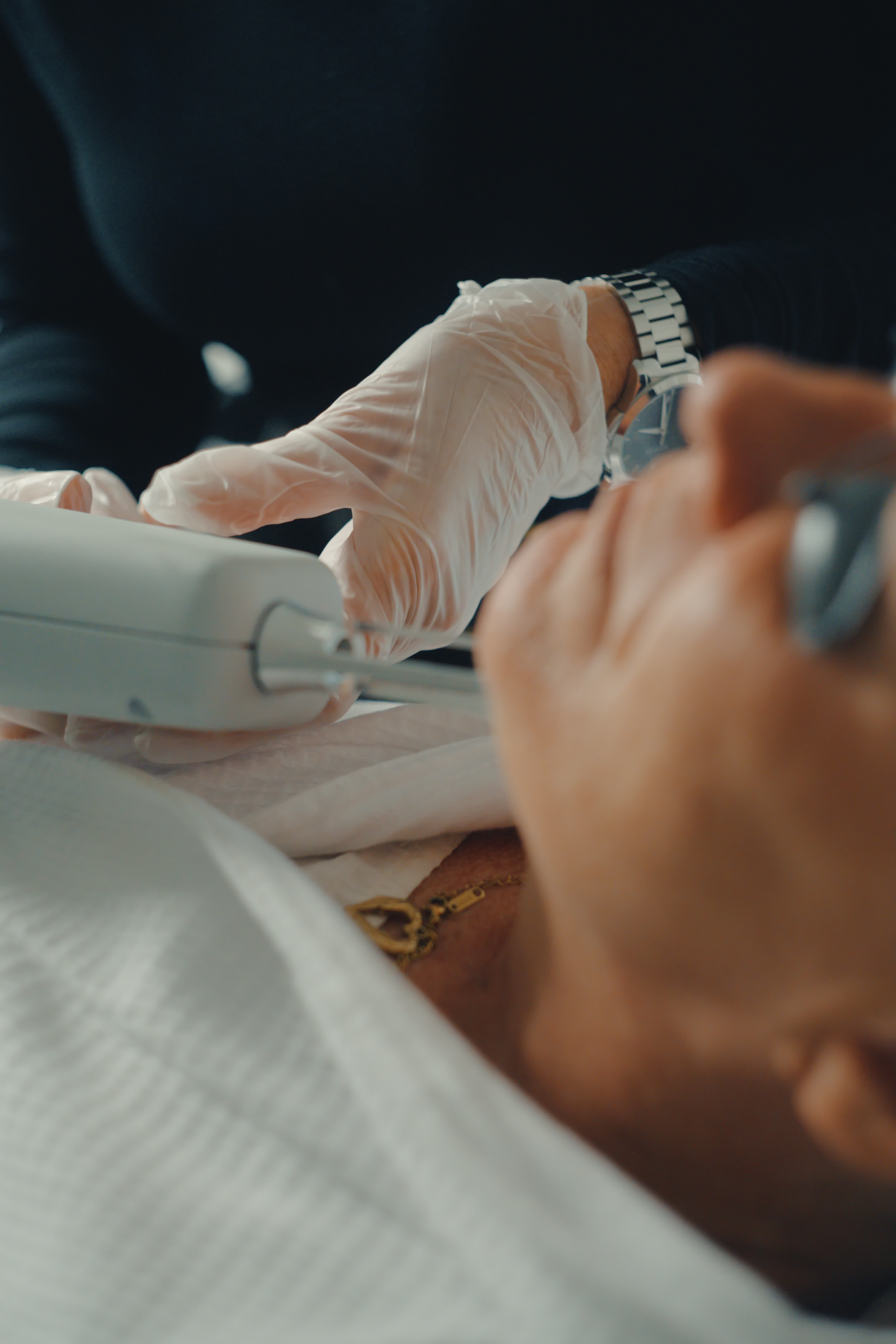 Person wearing gloves holding a cosmetic device on a person's face.