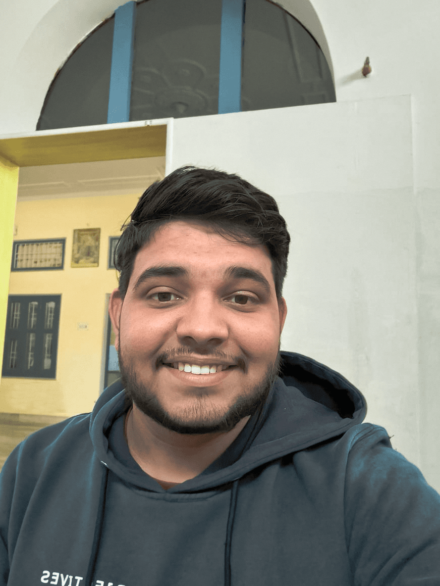 Person wearing a blue puffer jacket and red backpack standing in front of a light blue building on a city street.