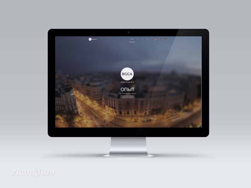 Pantalla de ordenador con diseño web BGCA y vista aérea de ciudad iluminada.