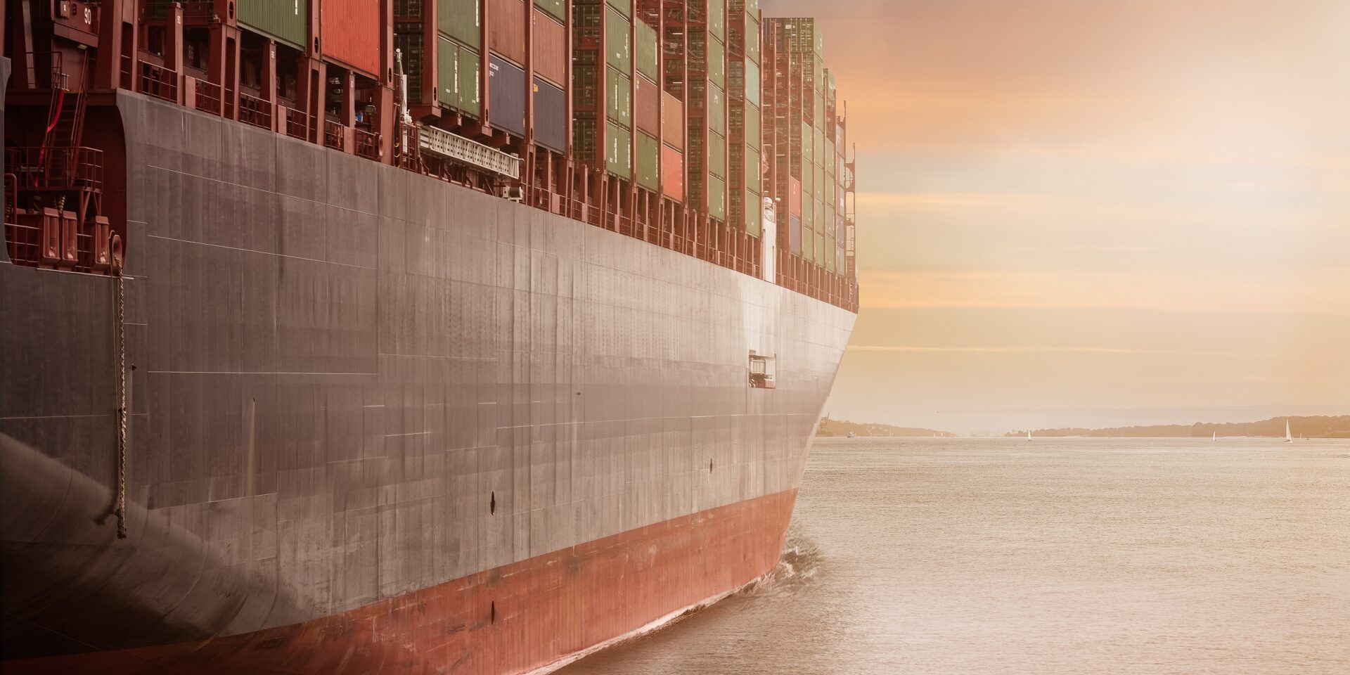 A massive cargo ship, loaded with colorful shipping containers, sails through calm waters at sunset, reflecting the warm, orange hues of the sky.