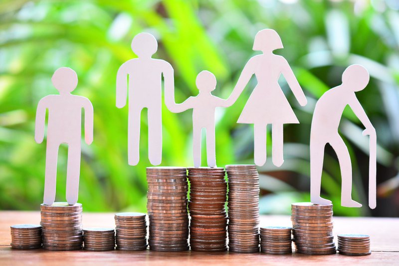 A paper cutout of people standing on stacks of coins in front of a background of greenery.