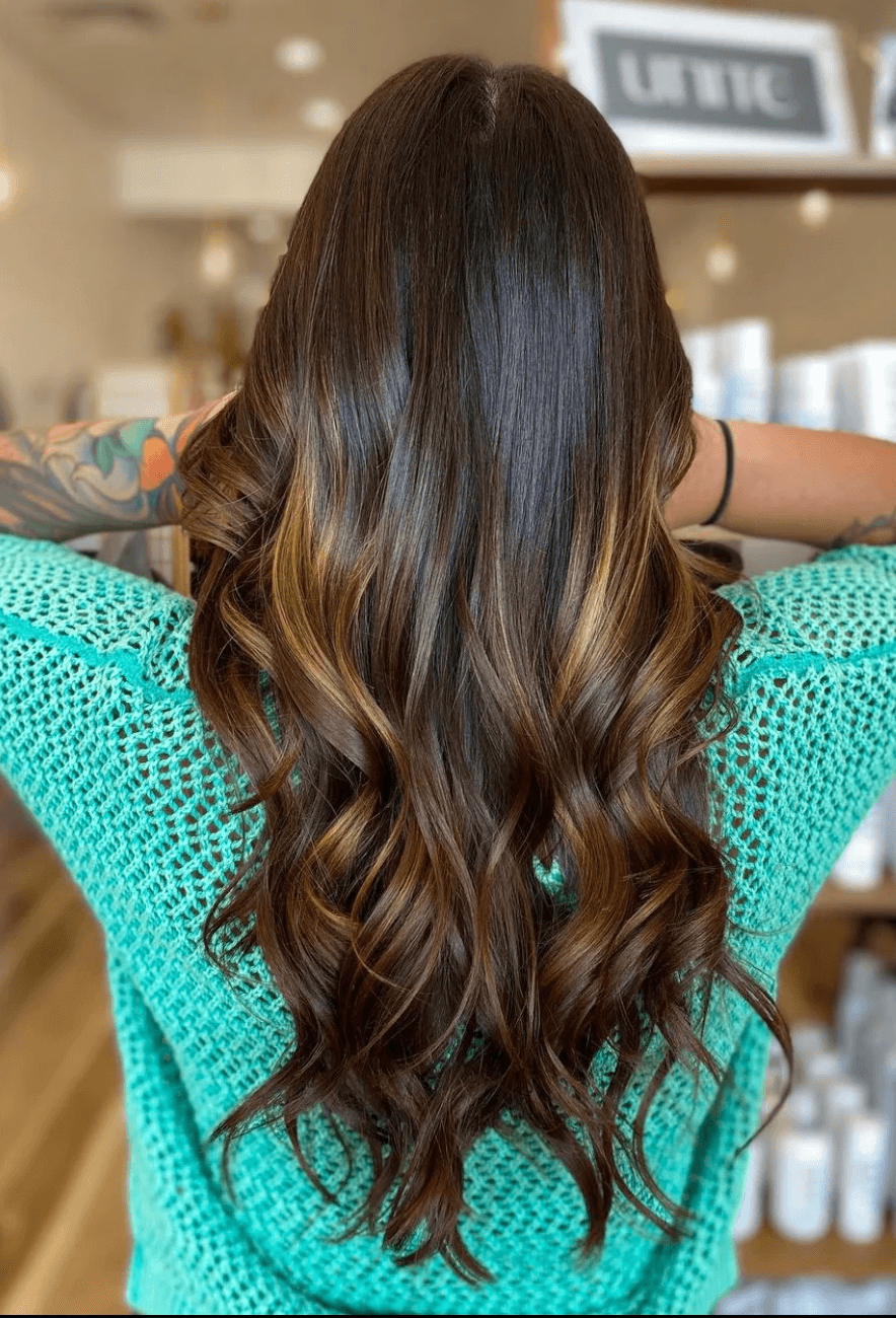 Back view of long, rich brunette hair with caramel balayage highlights, styled in soft beachy waves.