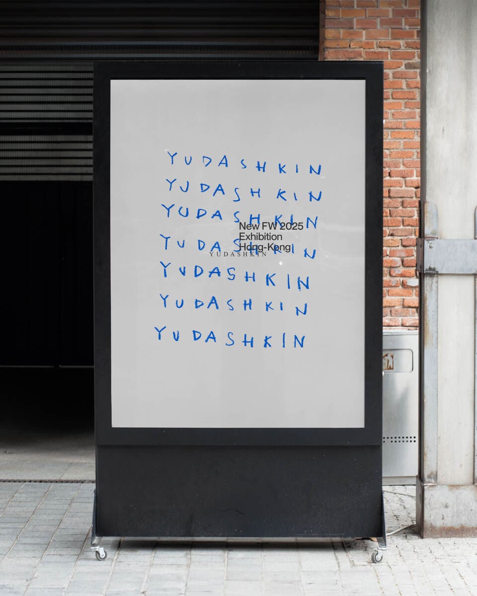 A billboard in the street with a design of a handwritten blue text that says yudashkin duplicated several times.