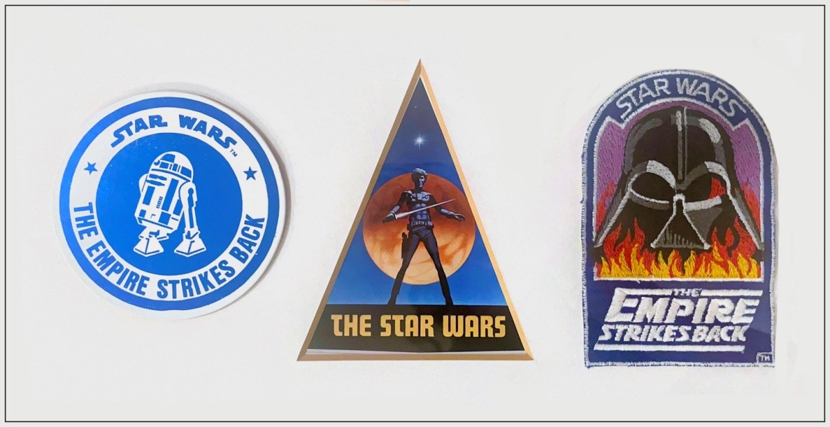 A collection of Star Wars memorabilia including an original triangular sticker, a coaster from the premiere of The Empire Strikes Back, and a cloth badge worn by cast and crew while filming in Norway.