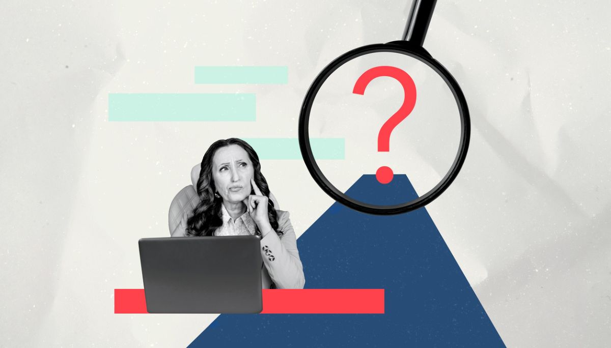 Person at desk with laptop under magnifying glass and question mark, symbolizing building hiring rubrics for consistent interviews.