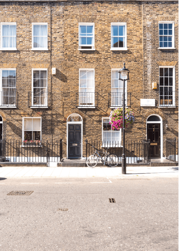 A serene outdoor seating area with two chairs, surrounded by lush greenery and a glassed-in structure.