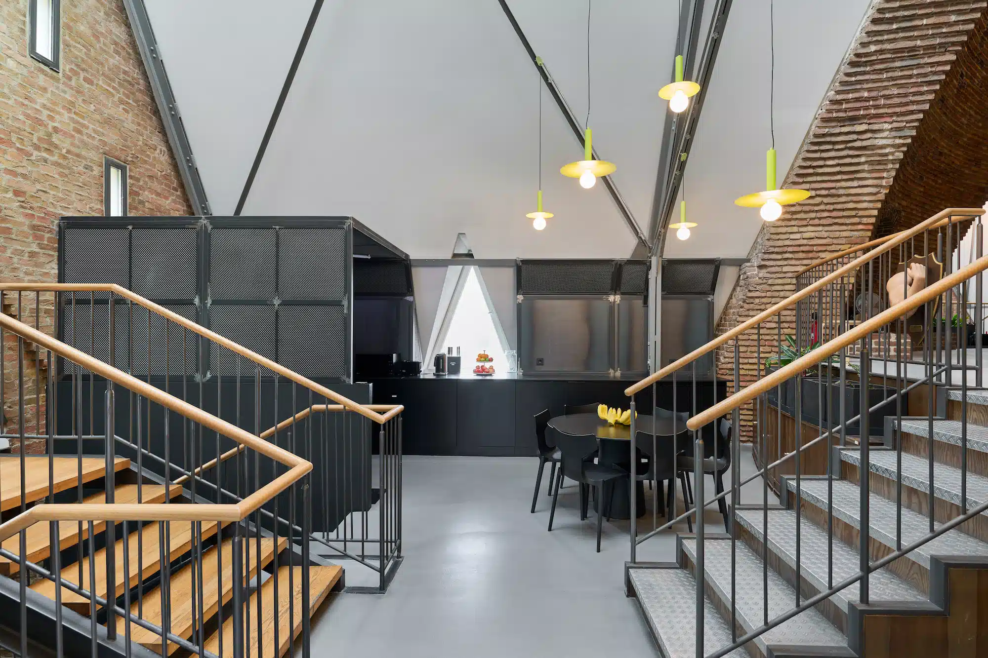 Dojo Office – main room with symmetrical double staircase, open kitchen and yellow pendant lights under a pitched roof
