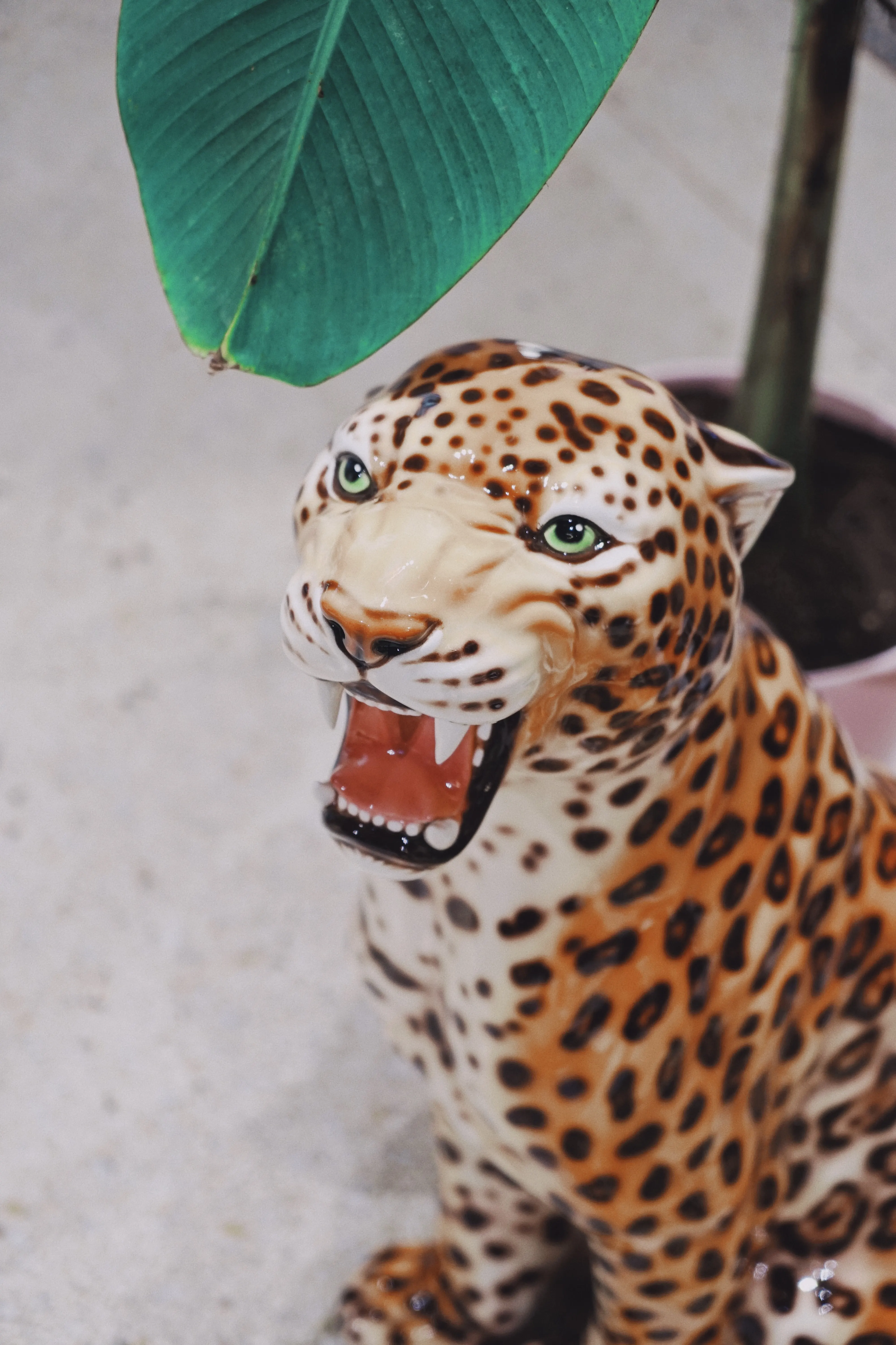 Close-up of a glossy ceramic leopard sculpture with open mouth under a banana leaf at UZWEI FASHION HOTEL.