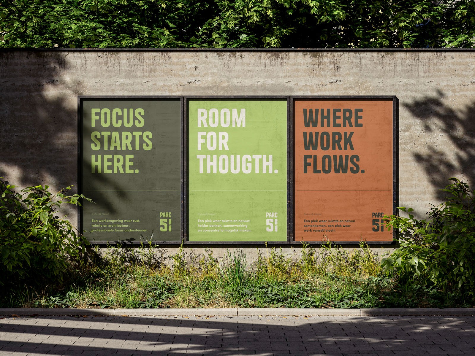 Drie grote outdoor posters naast elkaar op een grijze muur in een groene omgeving. De posters hebben de tekst "FOCUS STARTS HERE.", "ROOM FOR THOUGHT." en "WHERE WORK FLOWS." in strakke typografie op respectievelijk een donkergroene, lichtgroene en oranje achtergrond.