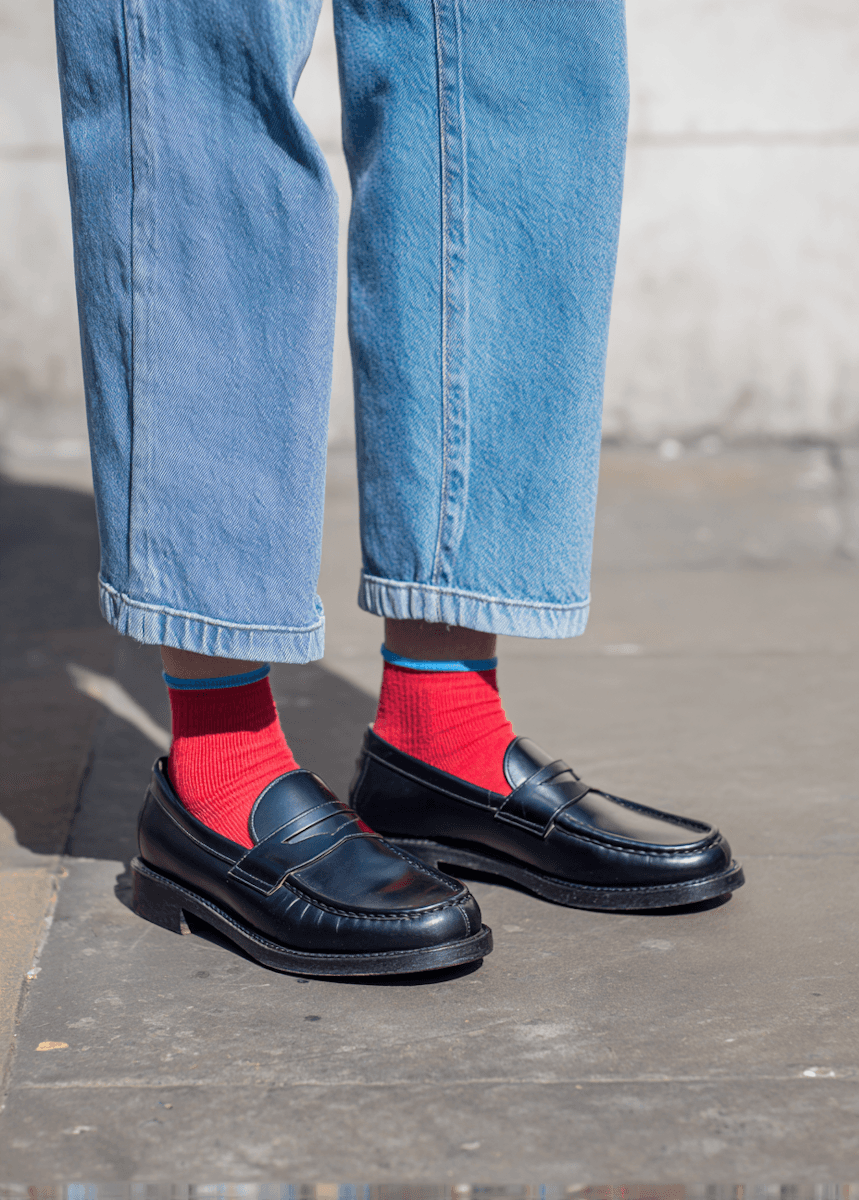 A person wearing red socks with black loafers and cropped jeans