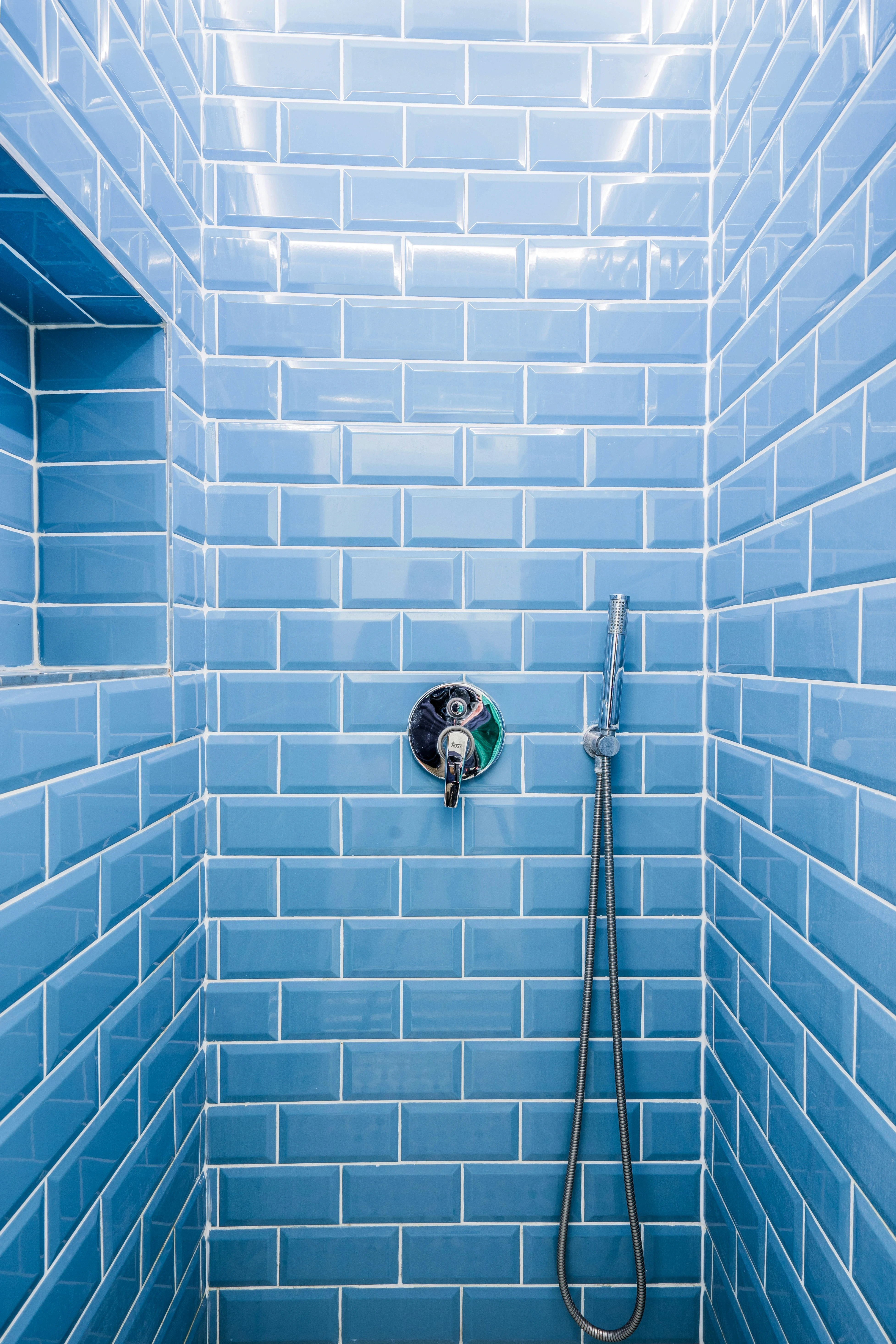 A modern shower featuring a blue tile wall and a sleek shower head, creating a refreshing bathing environment.