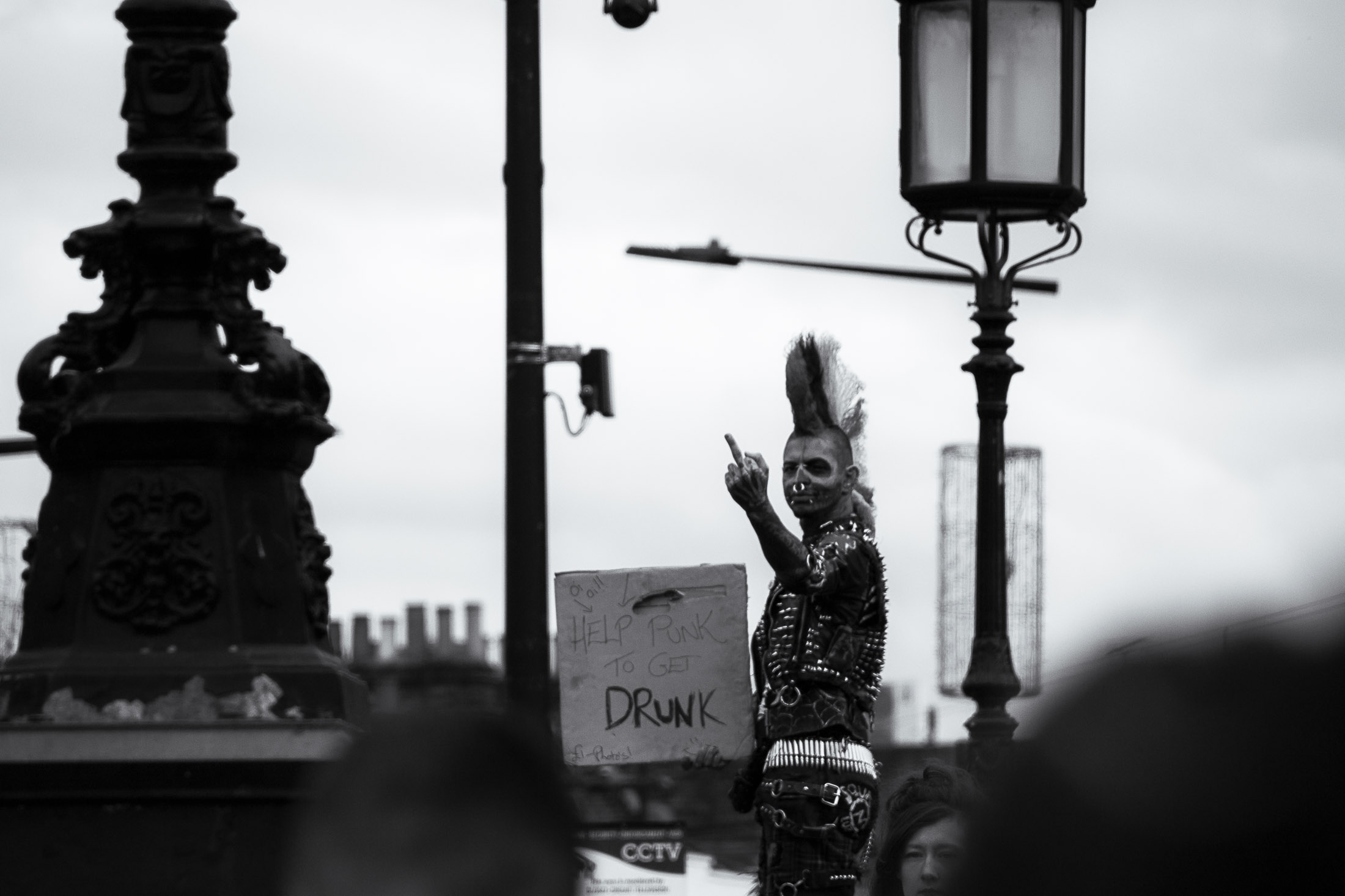 Black and white street photograph of a punk man with a mohawk holding a sign in an urban setting.