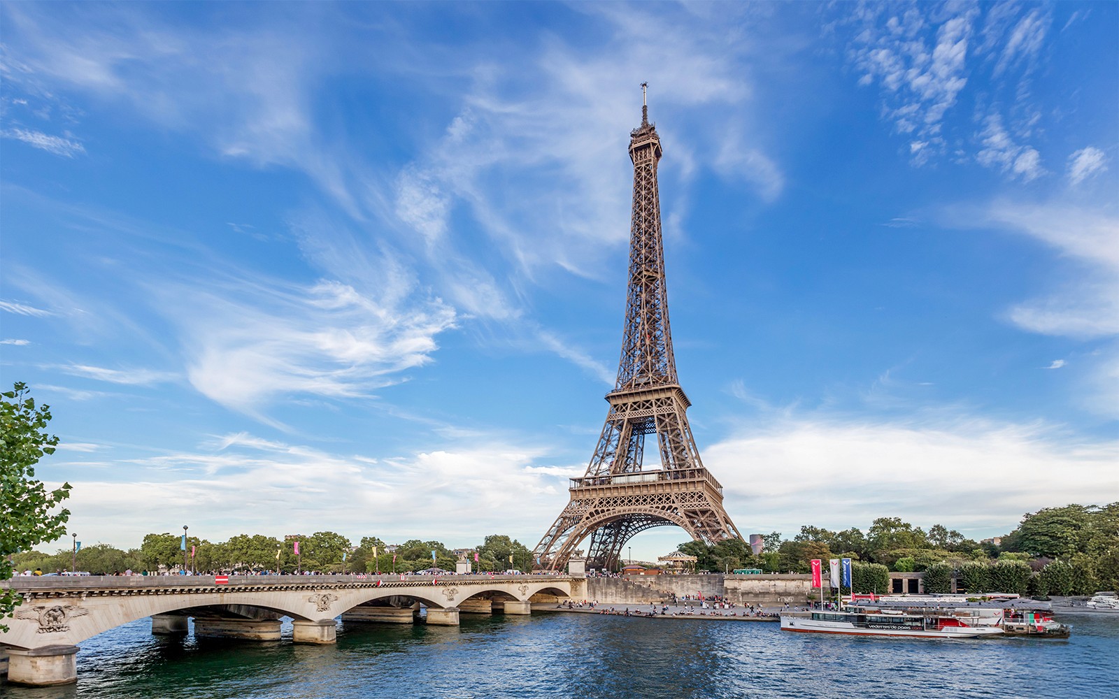 在巴黎塞纳河对岸欣赏埃菲尔铁塔的景色，一艘船正在经过。