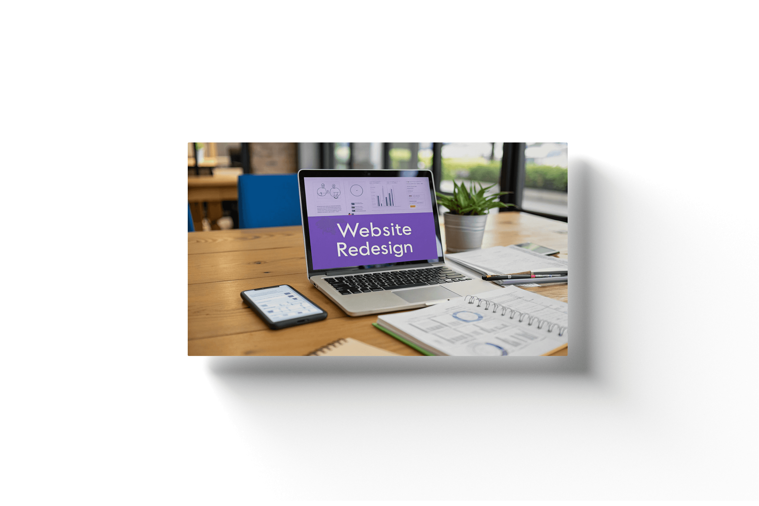 a laptop on a wooden desk with a purple screen and text reading 'website redesign' being shown