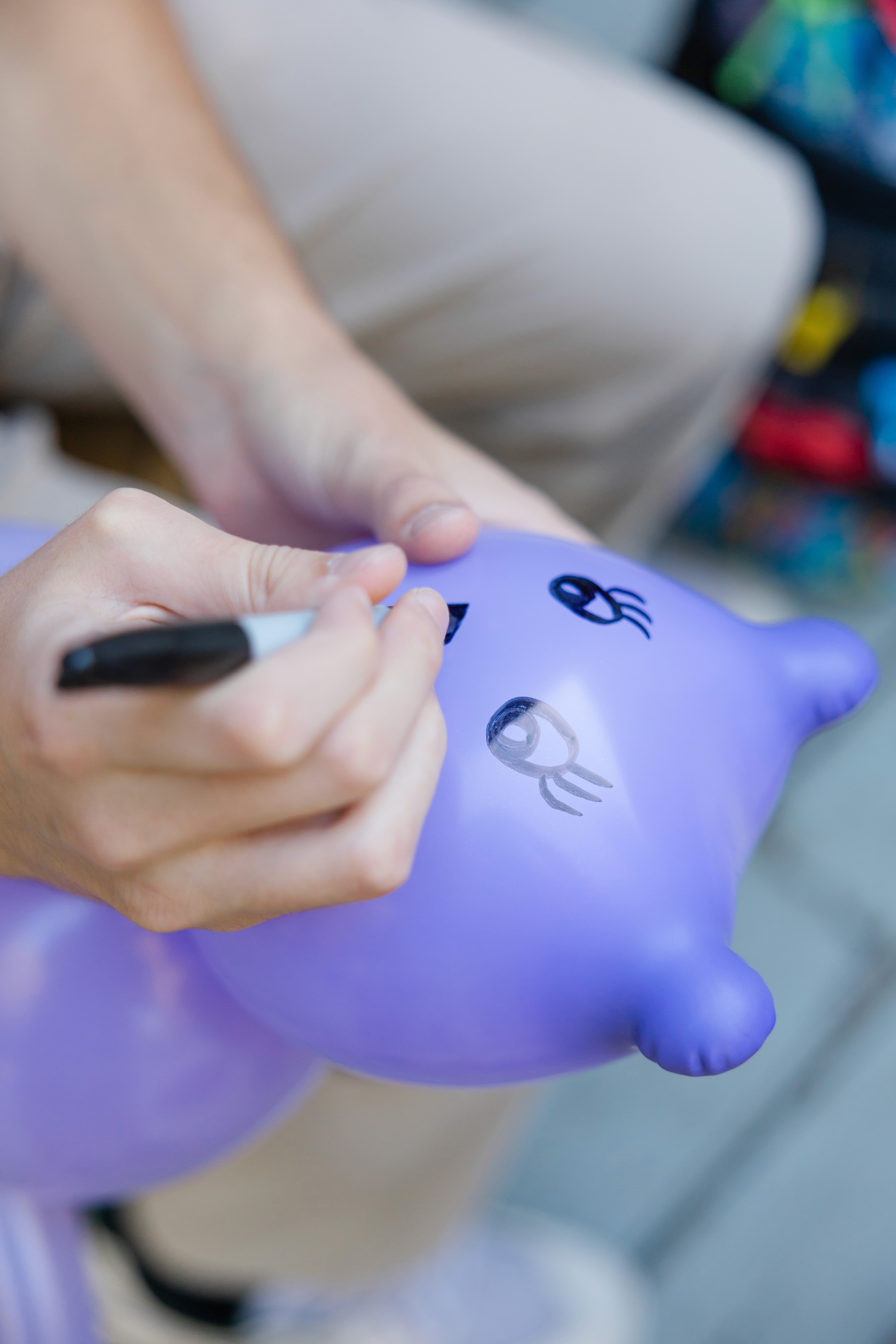 Close-up of hands drawing a cute face on a purple balloon bear with a black marker outdoors