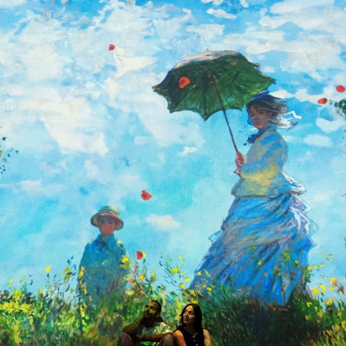 Two people sit in front of a large projection of a painting depicting a woman with an umbrella and a child in a field with flowers.